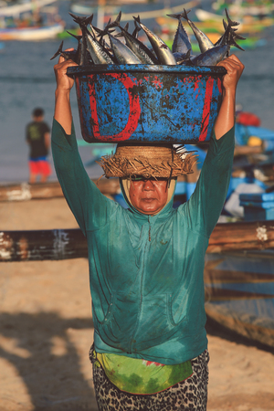 BALI, INDONESIA - AUGUST 6, 2017 : Balinese fishmonger carry fishes in basin at the morning market in Kedonganan - Passer Ikan, Jimbaran beachのeditorial素材