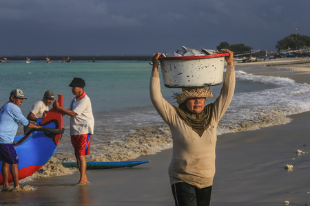 BALI, INDONESIA - AUGUST 6, 2017 : Balinese fishmonger carry fishes in basin at the morning market in Kedonganan - Passer Ikan, Jimbaran beachのeditorial素材
