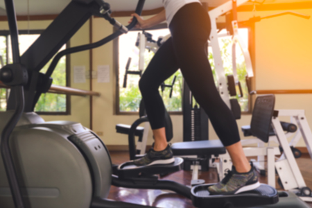 Blurred of young fit woman using an elliptic trainer in fitness centre,  Close up of legs of fitness girl in gymの写真素材
