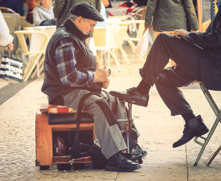 Lisbon, Portugal -  November 6, 2018: Shoeshine man unidentified working on client's shoe on a street in Lisbon, Portugal. Lisbon is very traditional in its ancient streets find shoeshineのeditorial素材