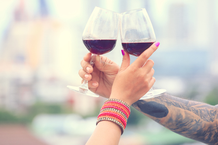 Close up on hands holding red wine glasses on balcony in vintage style, celebration conceptの写真素材