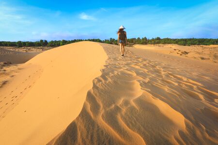 back side of woman walking on red sand dune in Mui ne, Vietnamの写真素材