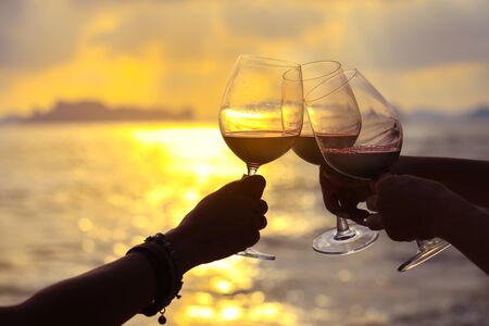 Close up on hands holding red wine glass on balcony during sunset, celebration conceptの写真素材
