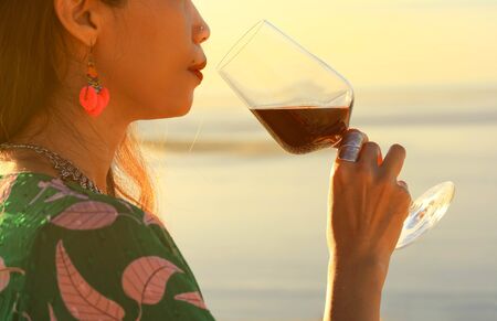 woman holding red wine glasse on the beach during sunset, celebration conceptの写真素材