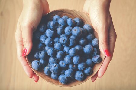 Top view of woman hands holding ripe blueberries on wooden bowlの写真素材