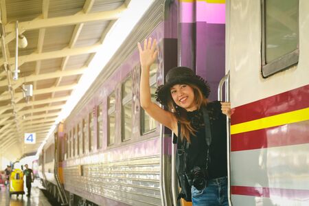 Traveler asian woman standing on train door while train is leaving the station. vacation concept