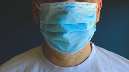 Half face man wearing medical blue mask during virus epidemic lockdown posing on blue wall.の写真素材