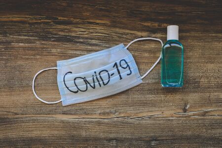 Medical mask with covid-19 printed on it and blue bottles of hand sanitiser on wooden backgroundの写真素材
