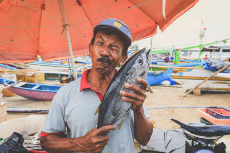 Bali Indonesia - February 6, 2020 : Happy Balinese fishmonger holdong tuna fish at seafood market in Kedonganan - Passer Ikan, Jimbaran beachのeditorial素材