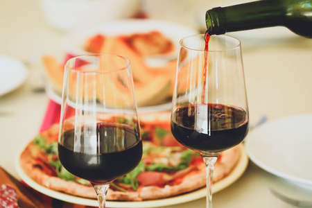 Pouring red wine from bottle into  glasses on table with food backgroundの写真素材