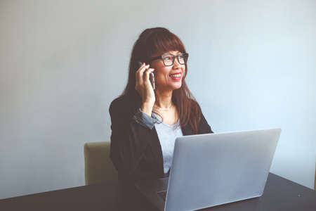 Pretty smiling asian woman using cell telephone and notebook at office