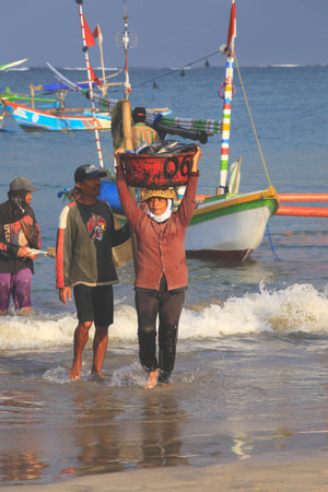 BALI, INDONESIA - AUGUST 6, 2017: Balinese fishmonger carry fishes in basin at the morning market in Kedonganan - Passer Ikan, Jimbaran beachのeditorial素材