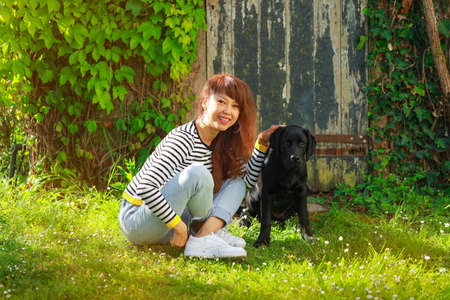 Asain woman cuddle her dog and sit on the green grass in summerの写真素材