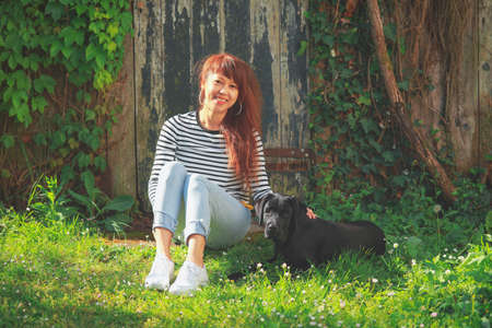 Asian woman cuddle her dog and sit on the green grass in summerの写真素材
