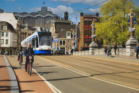 Amsterdam-Netherlands, April 18, 2017: Street scene with modern tram with tourists on bicycles in Amsterdam, tram is one of the quickest ways to get into and around the city centerのeditorial素材