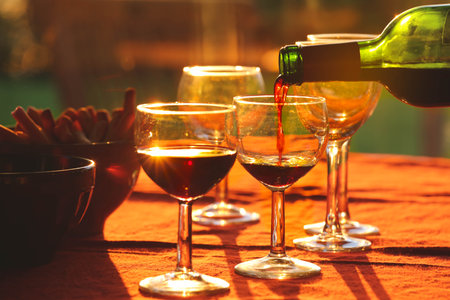 Pouring red wine from the bottle into glasses on the table with snacksの写真素材