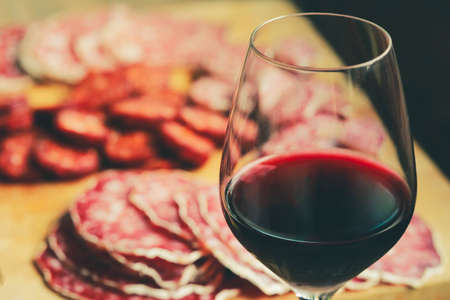 Selective focus on glass of red wine with traditional salami sliced on cutting boardの写真素材