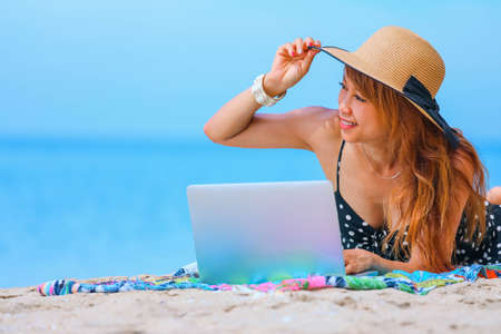 Attractive asian woman working on laptop on the tropical beach, holidays and vacation conceptの写真素材