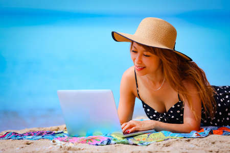 Attractive asian woman working on laptop on the tropical beach, holidays and vacation conceptの写真素材