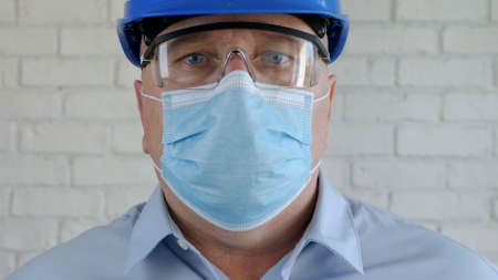 Engineer with Safety Helmet and a Protection Mask on His Face Talking to the Cell Phoneの写真素材