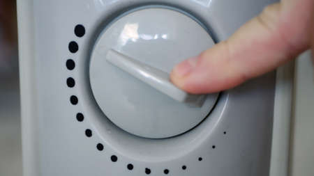 Man Sets the Heating Temperature of an Electric Radiator at Home in a Cold Roomの写真素材