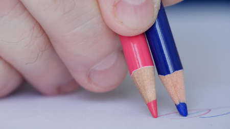 Image with a Person Drawing with Two Colored Pencils on a White Piece of Paper