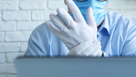 Doctor in a Hospital Office with a Face Mask and Protective Gloves Using a Laptopの写真素材