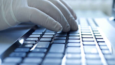 Closeup Image with Hands Wearing Protective Gloves Using the Laptop Keypadの写真素材