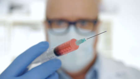 Doctor Wearing Protecting Gloves and Face Mask Keeping in Hand an Injectionの写真素材