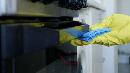 Closeup Image with Person Hands Wearing Protective Yellow Household Gloves in the Kitchen and Cleaning a Stoveの写真素材