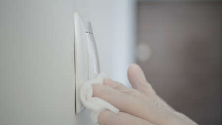 Image with Man Hands Wearing Medical Gloves Disinfecting a Lights Switch Using a Wet Wipe and Disinfectant Solutionの写真素材