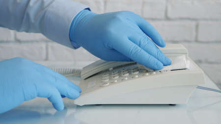 Image with Hands Wearing Protective Gloves Cleaning with a Clean Wipe and Medical Disinfectant a Desk Telephoneの写真素材