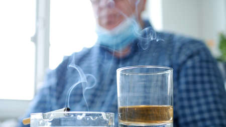 Blurred Image with a Man who Drinks Alcohol and Smokes a Cigarette Wearing Protective Mask on His Facetective Mask on His Faceの写真素材
