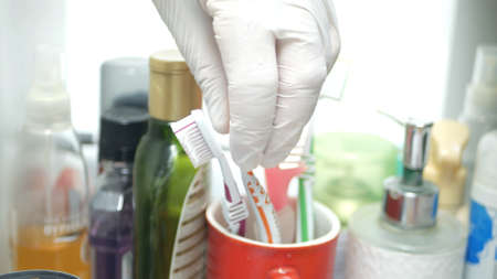 Hand Protected by Glove Takes a Toothbrush from the Bathroom Cabinet Drawerの写真素材