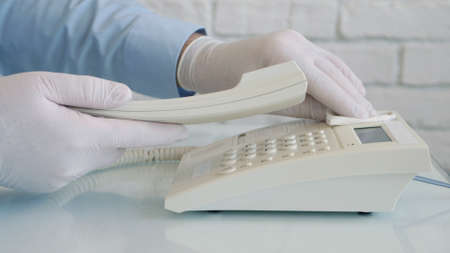 Man Wearing Protection Gloves in Hands Cleaning and Disinfecting a Telephone Using a Spray and Wet Wipesの写真素材