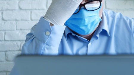 Doctor in a Hospital Office with a Face Mask and Protective Gloves Using a Laptopの写真素材