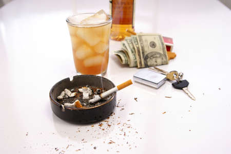 Questionable lifestyle concept with alcohol, cigarettes, money, and car keys on dirty tableの写真素材
