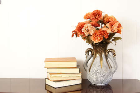 Vase of silk flowers next to stack of old hardback books.の写真素材