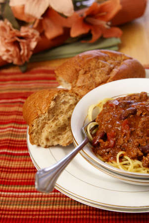 Western style meat and bean chili served on top of spaghetti with a side of rustic wheat bread.の写真素材