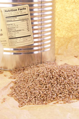 Small pile of whole wheat grains with nutrition label on can behind.の写真素材