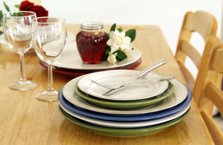 Stacked plates on a golden wood dinner table with chairs, wine glasses, candle and flowersの写真素材