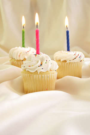Birthday candles on small cupcakes with whipped cream icing and candy sprinkles.の写真素材