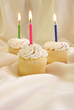 Birthday candles on small cupcakes with whipped cream icing and candy sprinkles.の写真素材
