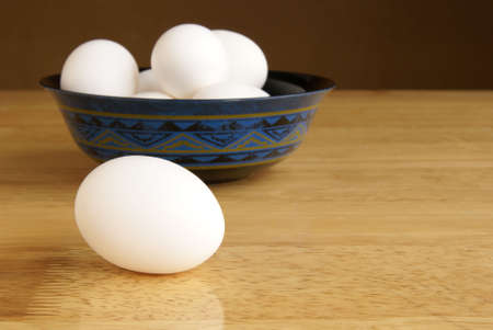 Whole egg laying on a butcher block table with a bowl of eggs in the backgroundの写真素材