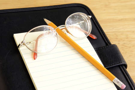 Eyeglasses, pencil and notepad sitting on top of black leather portfolio or schedule book