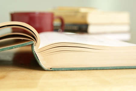 Old open hardback book laying on a table with blurred books and coffee cup in the backgroundの写真素材