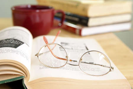 Eyeglasses on open book with coffee and other books stacked in the background.の写真素材