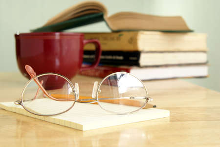 Eyeglasses on a yellow notepad with books and coffee behindの写真素材