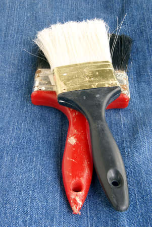 Two old dirty paintbrushes laying on denim fabric
