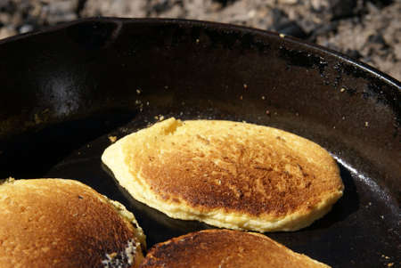 Cornmeal pancakes cooking in a cast iron skillet over an open fire outdoors. Close up view of cakesの写真素材